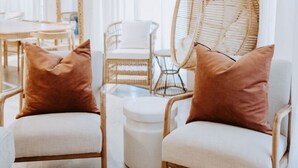 Une pièce meublée de blanc, avec notamment deux chaises dotées de coussins marron, un fauteuil en osier et une table blanche.