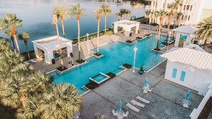 Un espace piscine doté de chaises longues et d’un kiosque, entouré de palmiers et bordé d’une étendue d’eau.