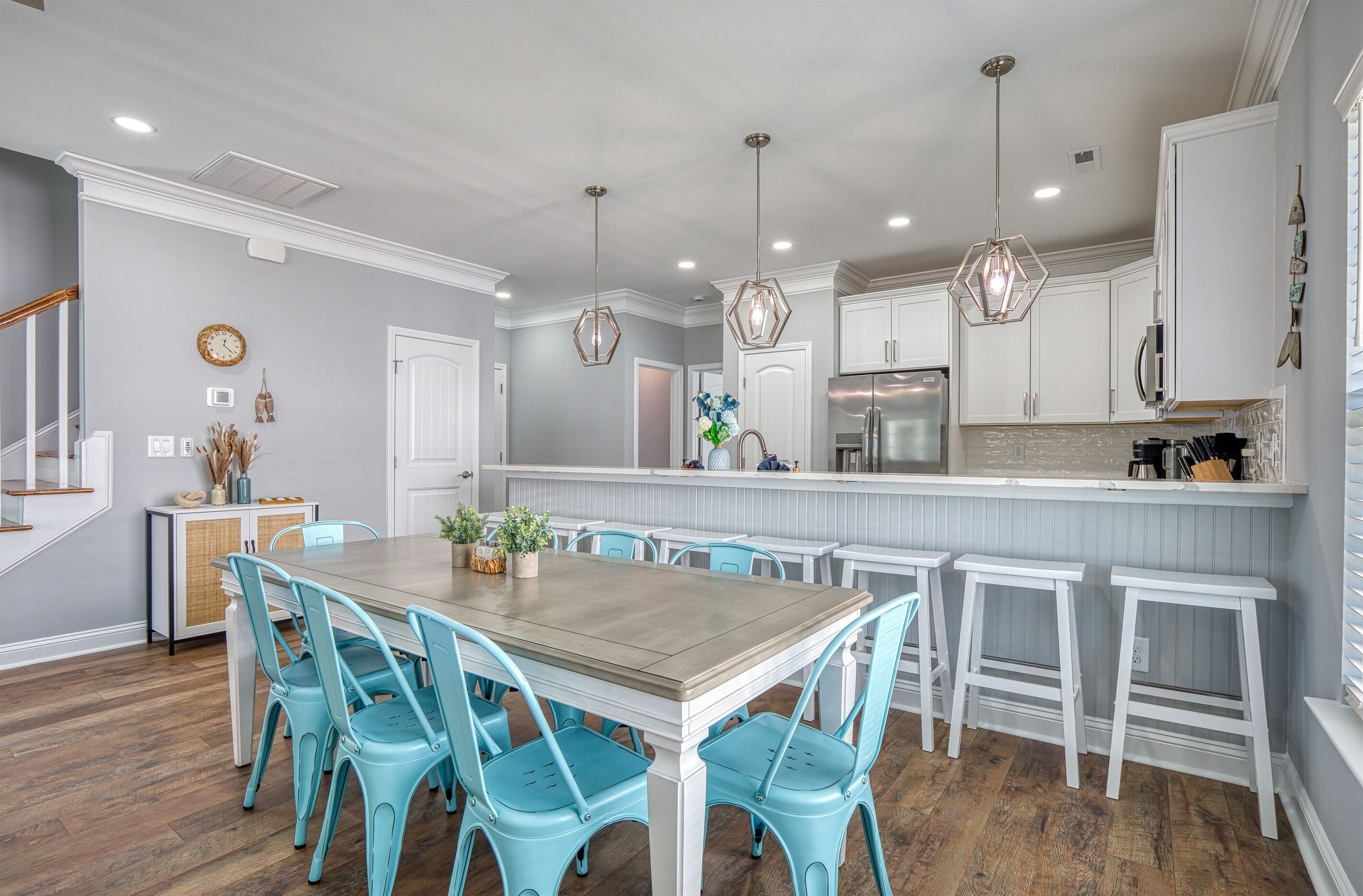 A modern kitchen with white cabinets, a wooden dining table, and blue chairs.