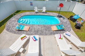 Ein Gartenpool mit einer Steinterrasse, umgeben von weißen Liegestühlen und einem kleinen Basketballkorb.