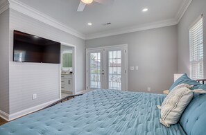 Ein Schlafzimmer mit einem großen Bett, einem Deckenventilator und einer Tür, die auf einen Balkon führt.