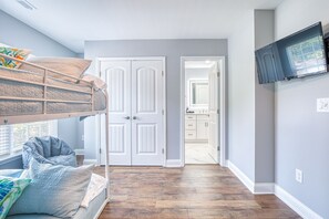 Cozy bedroom with a bunk bed and single bed, featuring a television and door to a hallway.