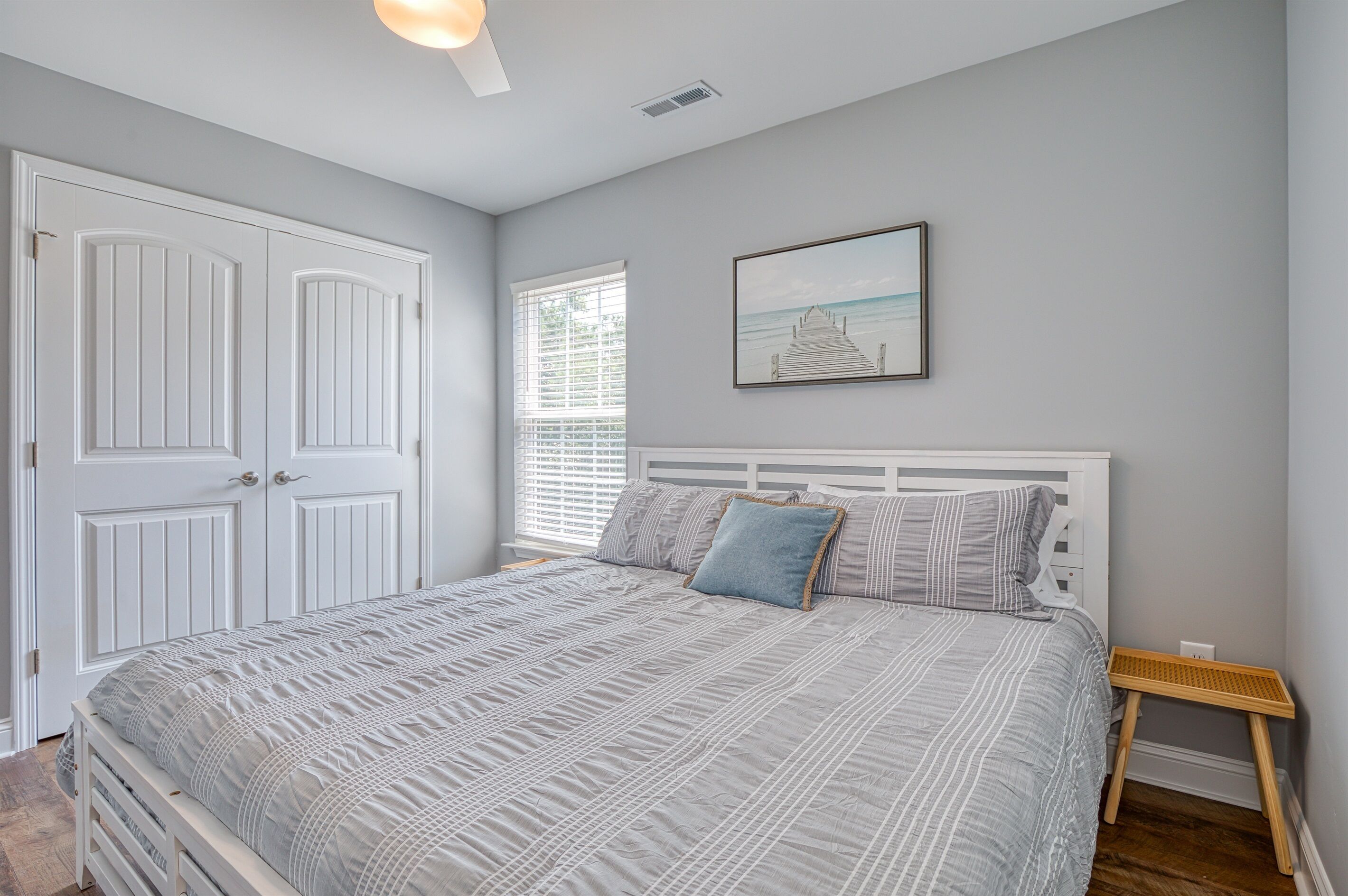 A bedroom with a bed, a window with blinds, a door, and a framed picture on the wall.