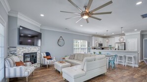 A modern living room with a fireplace, a large sofa, and a dining area with a kitchen in the background. - Beach Home! Private Pool! Arcade-Beach-FUN! Elevator (Murrells Inlet)