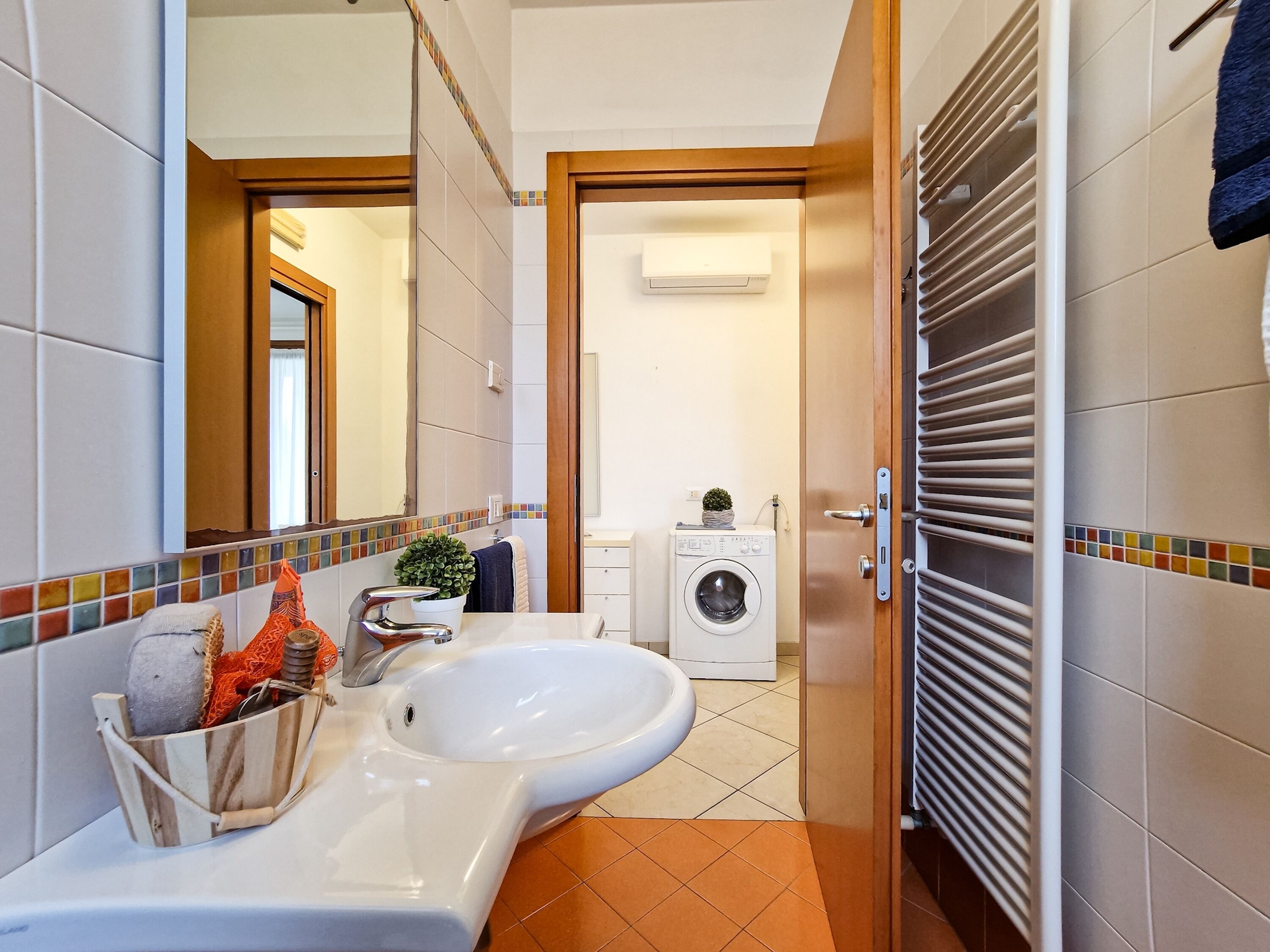 Ein Badezimmer mit Waschbecken, Spiegel und einer Waschmaschine im Hintergrund.
