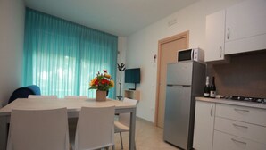 A modern kitchen with a refrigerator, microwave, and a dining area with chairs and a table. - Elegant Apartment Near the Beach (Rosolina)