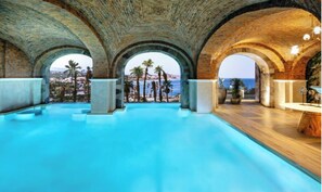 Una piscina interior con techos arqueados y vistas a palmeras y al mar.