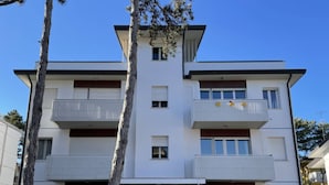 A multi-story residential building with balconies, a central entrance, and a small front garden. - Spacious Family Apartment for 8 Guests (San Michele al Tagliamento)