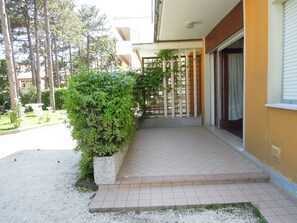 En bostadsbyggnad med en stenlagd entré, en liten trädgårdsyta med en häck och ett trästaket.