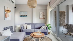 A modern living room with a grey sofa, a round coffee table, and a hanging rattan light fixture. - Sanders Old Port - Cozy 1-bdr. Apt. w/ Balcony (Thessaloniki)