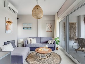 Ett modernt vardagsrum med en grå soffa, ett runt soffbord och en hängande lampa av rotting.