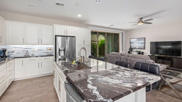 A modern kitchen with white cabinets, a stainless steel refrigerator, and a marble countertop. - Gilbert Haven: A Family Delight in Enchanting Community (Gilbert)