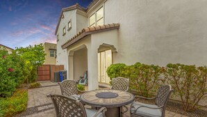 An outdoor patio with a round table and four chairs, surrounded by a garden and a building with a white exterior and a brown roof. - Gilbert Haven: A Family Delight in Enchanting Community (Gilbert)
