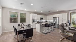 A modern kitchen with white cabinets, stainless steel appliances, and a central island with bar stools. - Gilbert Haven: A Family Delight in Enchanting Community (Gilbert)