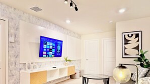 Een moderne woonkamer met een flatscreen televisie aan de muur, een glazen salontafel, een bank en een decoratieve lamp.