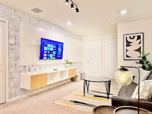Ein modernes Wohnzimmer mit einem wandmontierten Flachbildfernseher, einem Glastisch, einer Couch und einer dekorativen Lampe.