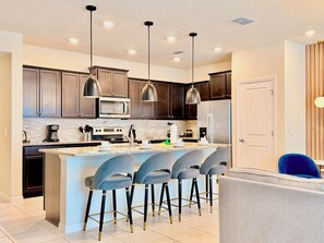 A modern kitchen with dark wood cabinets, stainless steel appliances, and a central island with bar stools. - Steps from Clubhouse! 5BR Townhome w/ Private Pool & Themed Rooms (Davenport)