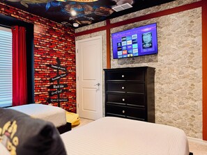 A hotel room with a brick wall, a television displaying channel options, a black dresser, and two beds. - Steps from Clubhouse! 5BR Townhome w/ Private Pool & Themed Rooms (Davenport)