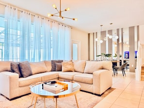 A modern living room with a sectional sofa, a glass coffee table, and a dining area with a view.