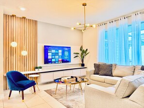 A modern living room with a flat-screen TV, a blue chair, a beige sofa, and a coffee table. - Steps from Clubhouse! 5BR Townhome w/ Private Pool & Themed Rooms (Davenport)