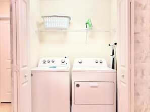 A laundry room with two front-loading washers and dryers, a white basket on a shelf, and a green iron. - Steps from Clubhouse! 5BR Townhome w/ Private Pool & Themed Rooms (Davenport)