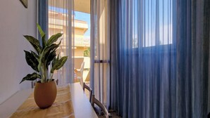 Ein Zimmer mit Esstisch, einer Topfpflanze und Blick auf einen Balkon mit Gartenmöbeln.