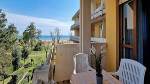Ein Balkon mit Tisch und Stühlen mit Blick auf Strand und Grünfläche.