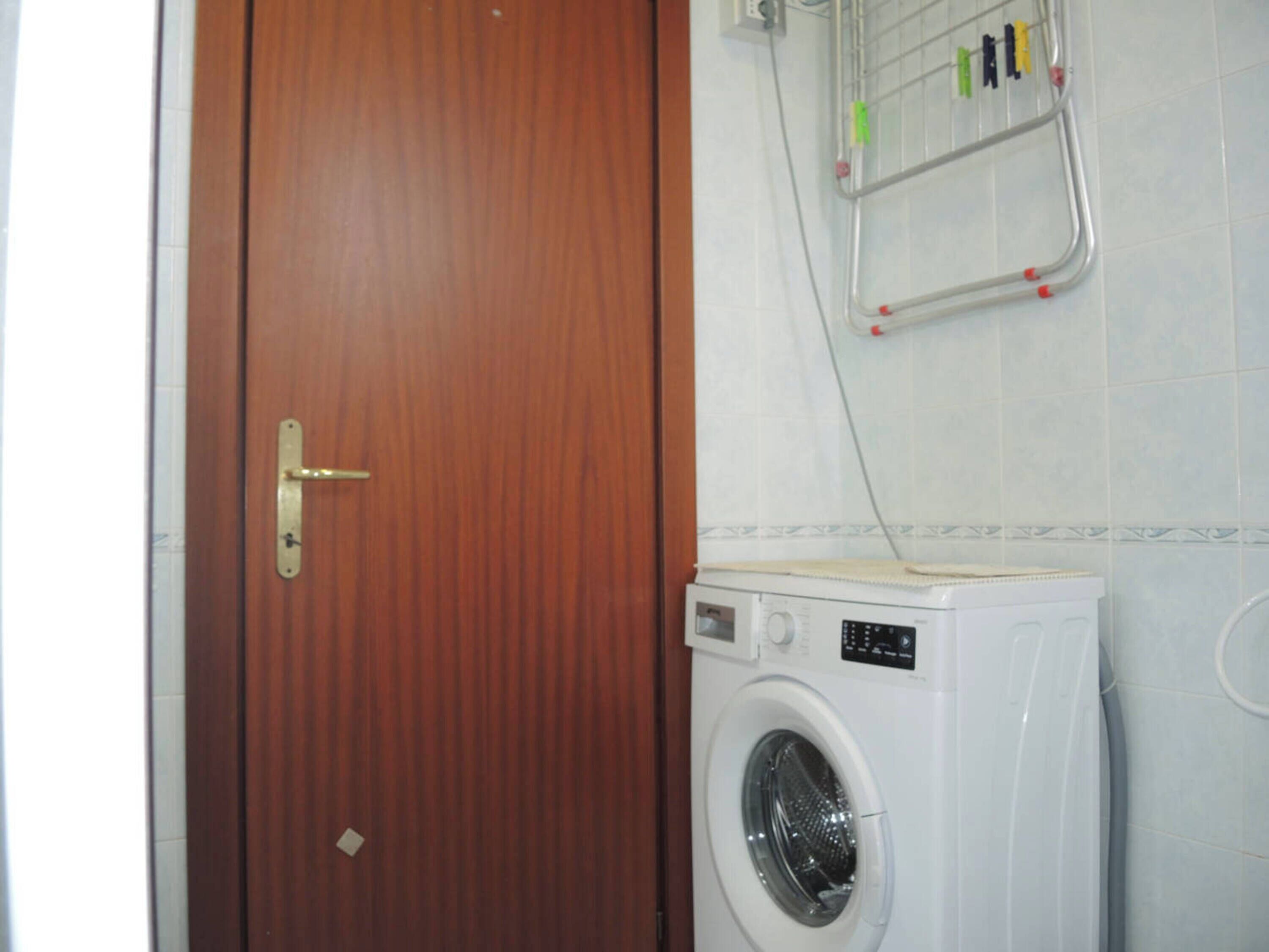 Quarto com porta de madeira, máquina de lavar e varal com roupas.