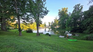 A grassy area with a lake, trees, and a small dock with a kayak. - Anglers Paradise (Dayton)