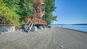 Ein hölzerner Aussichtsturm mit Wendeltreppe, der an einem kiesigen Strand mit freiem Blick auf das Wasser steht.