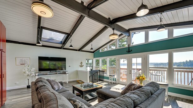 Ein geräumiges Wohnzimmer mit einer großen Couch, einem Couchtisch und einem Fernseher. Große Fenster und ein Balkon mit Blick sind vorhanden.