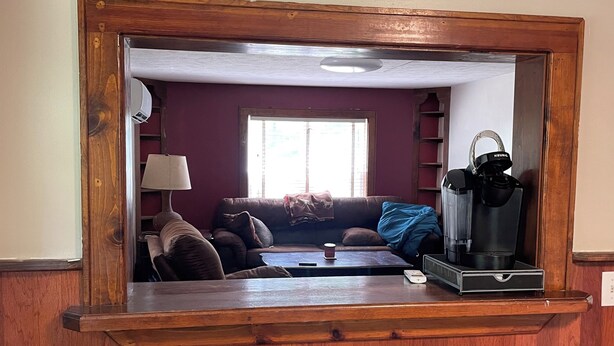 Una habitación con un espejo grande, paneles de madera, un sofá, una cafetera y dos taburetes.