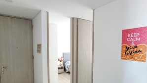 A hallway with wooden flooring leading to a bedroom with a bed and a nightstand. - Rolo Apartamentos Amoblados Jerez (Bogotá)