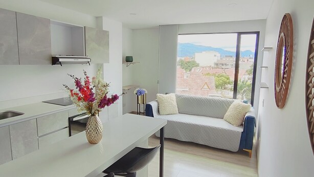 A modern kitchen with a dining area, a sofa, and a view of the cityscape. - Rolo Apartamentos Amoblados Jerez (Bogotá)