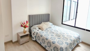 A bedroom with a bed, a nightstand, a vase with flowers, and a large window. - Rolo Apartamentos Amoblados Jerez (Bogotá)