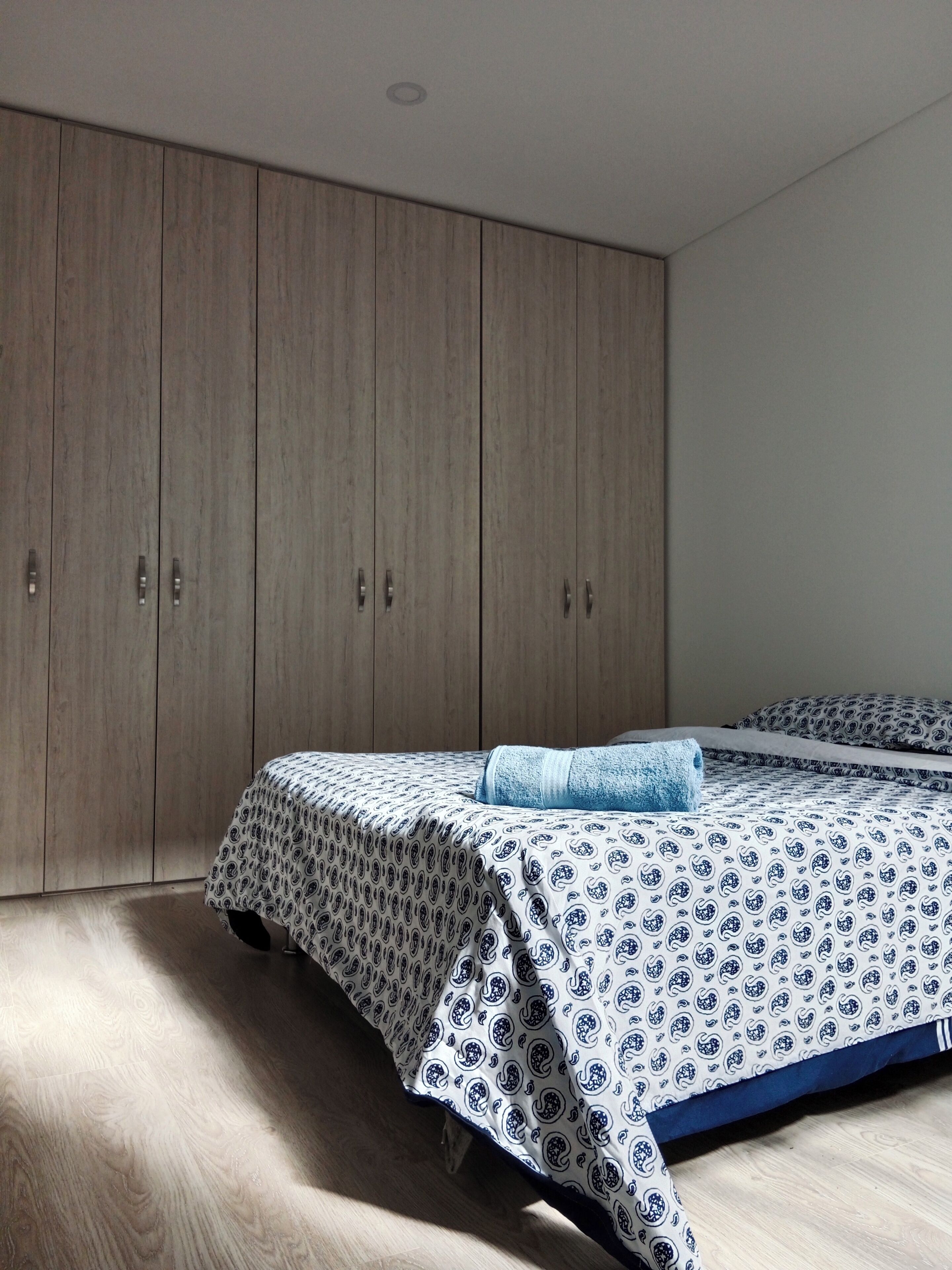 Ein Schlafzimmer mit großem Kleiderschrank, einem Bett mit gemusterten Textilien und Holzboden.