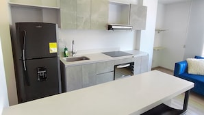 A modern kitchen with a white countertop, black chairs, a black refrigerator, and a built-in oven. - Rolo Apartamentos Amoblados Jerez (Bogotá)