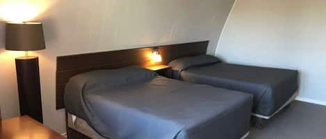 A hotel room with two beds, a nightstand, and a lamp.