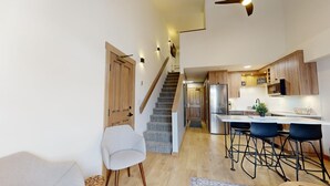 A modern kitchen with wooden cabinets, a stainless steel refrigerator, and a bar area with stools. - Hearthstone Lodge #332 (Sun Peaks)
