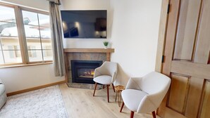 A living room with a fireplace, two armchairs, a sofa, and a TV mounted above the fireplace. - Hearthstone Lodge #332 (Sun Peaks)