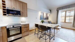 A modern kitchen with wooden cabinets, a built-in oven, and a dining area with a white table and black chairs. - Hearthstone Lodge #332 (Sun Peaks)