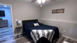 A bedroom with a bed, a ceiling fan, a wall-mounted TV, and a hallway leading to another room. - Home In Eddyville (Eddyville)