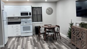 A modern kitchen with white cabinets, a microwave, and an oven. There's a dining area with a table and chairs, and a TV mounted on the wall. - Home In Eddyville (Eddyville)