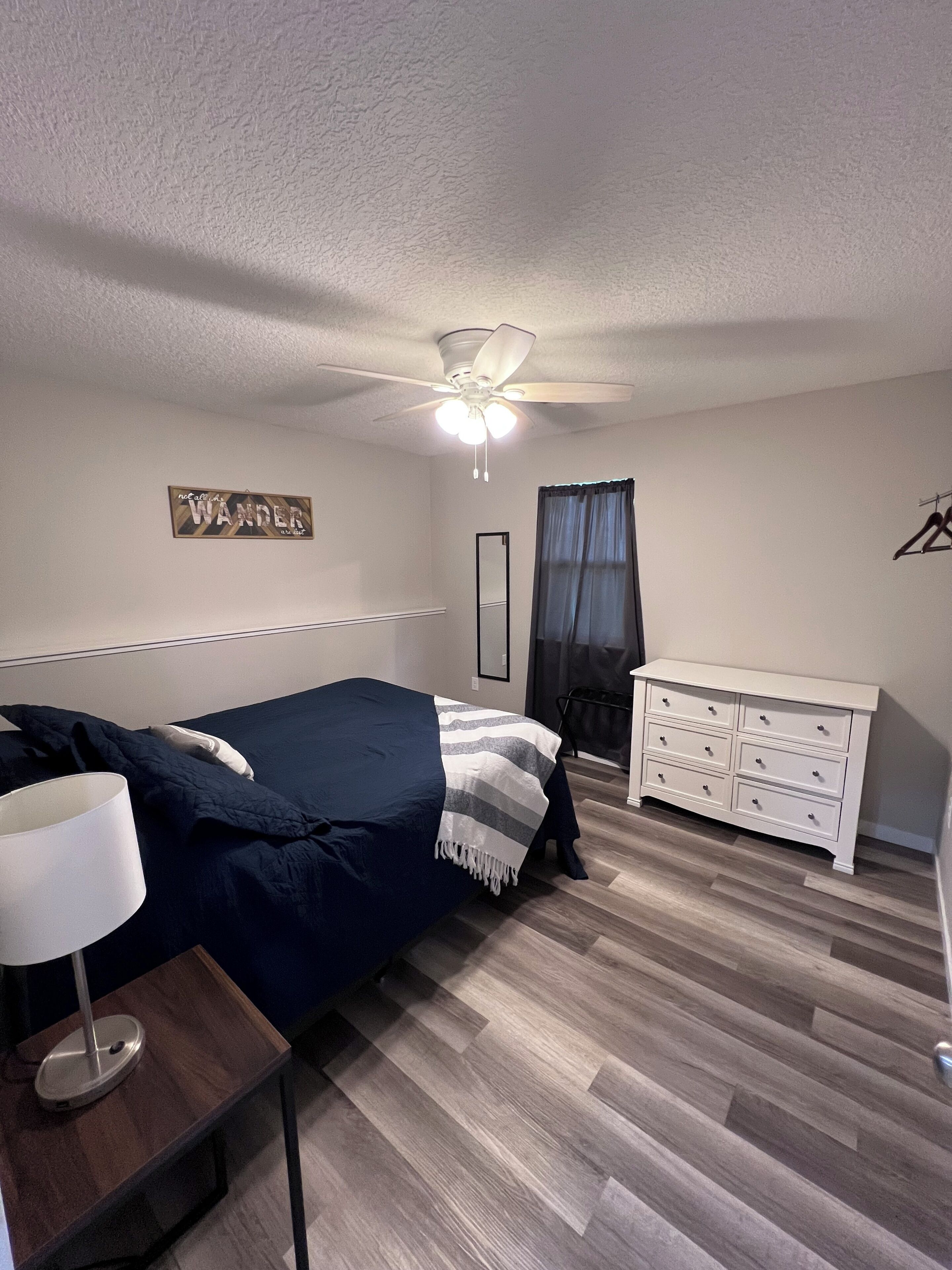 A bedroom with a bed, a dresser, a ceiling fan, and a wall-mounted mirror.