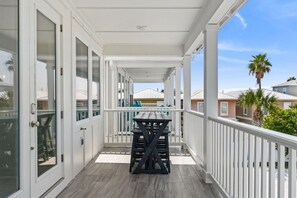 Eine überdachte Veranda mit Tisch und Stühlen, weißen Geländern und Blick auf benachbarte Häuser.