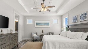 Una camera da letto con un letto, una sedia, una cassettiera, una ventola a soffitto e opere d'arte alle pareti.