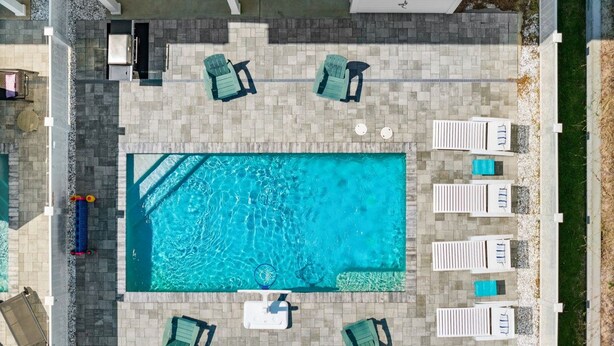 An aerial view of a rectangular swimming pool surrounded by lounge chairs and a deck area. - Private Pool, 30A Life in PCB, Laguna Beach Pearl (Panama City Beach)