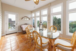 Ein Essbereich mit Glastisch und Korbstühlen, große Fenster mit Blick auf Grünflächen, eine Korbschaukel und eine Deckenleuchte.