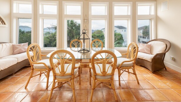 Una habitación luminosa con ventanas amplias, mobiliario de mimbre y una mesa de vidrio.