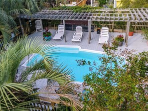 Ein Poolbereich mit einer Pergola, Liegestühlen und Topfpflanzen.